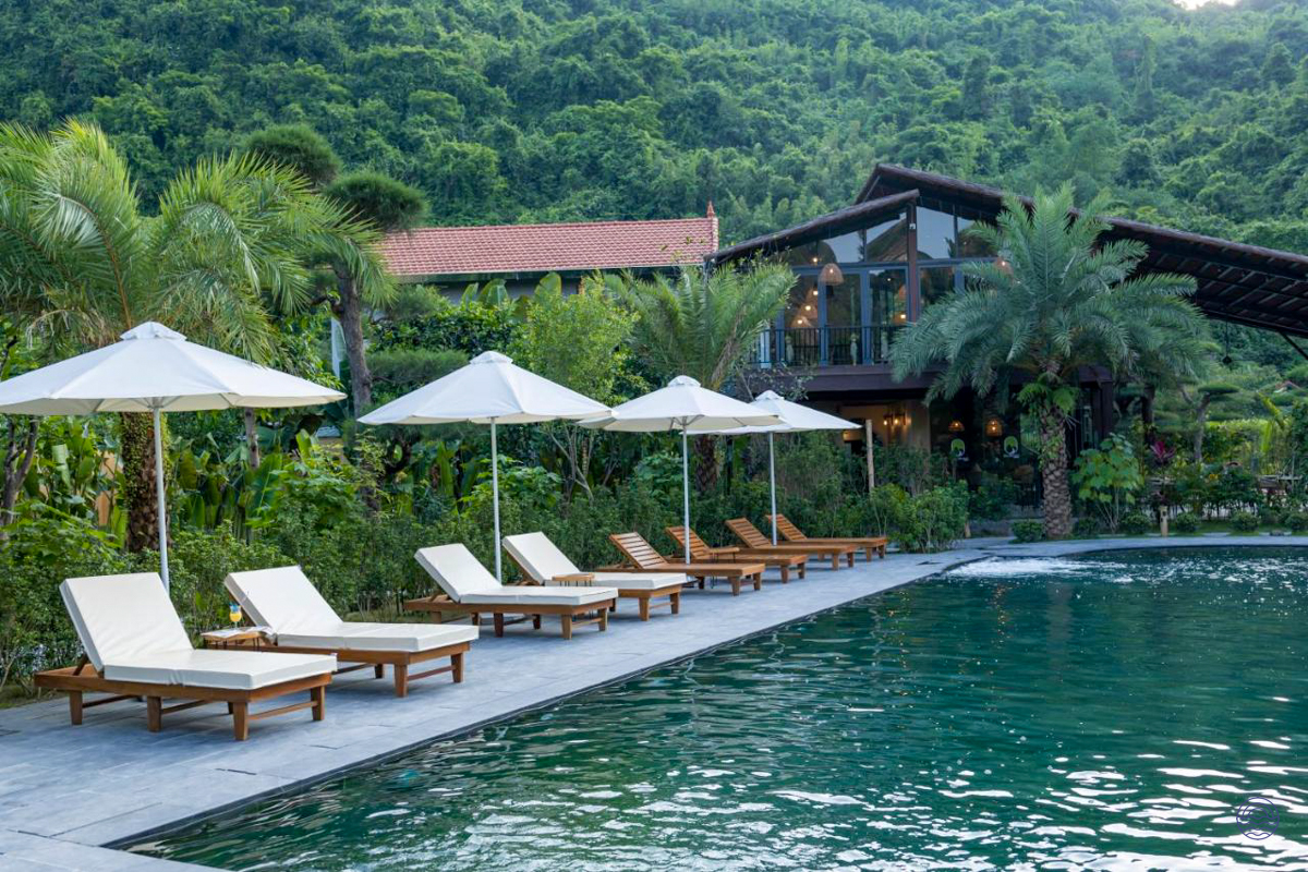 A serene swimming pool at Tam Coc Retreat, surrounded by lush tropical gardens and a forested mountain.