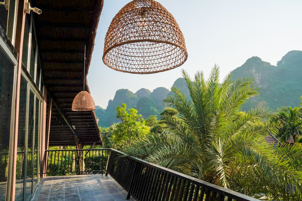A tranquil balcony view from Tam Coc Retreat, featuring lush palms and dramatic limestone karsts.