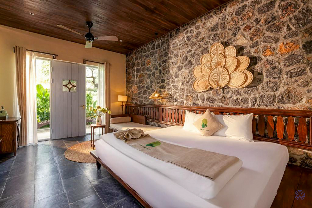 A spacious bedroom at Tam Coc Retreat with a large bed, rustic stone wall, and garden access.