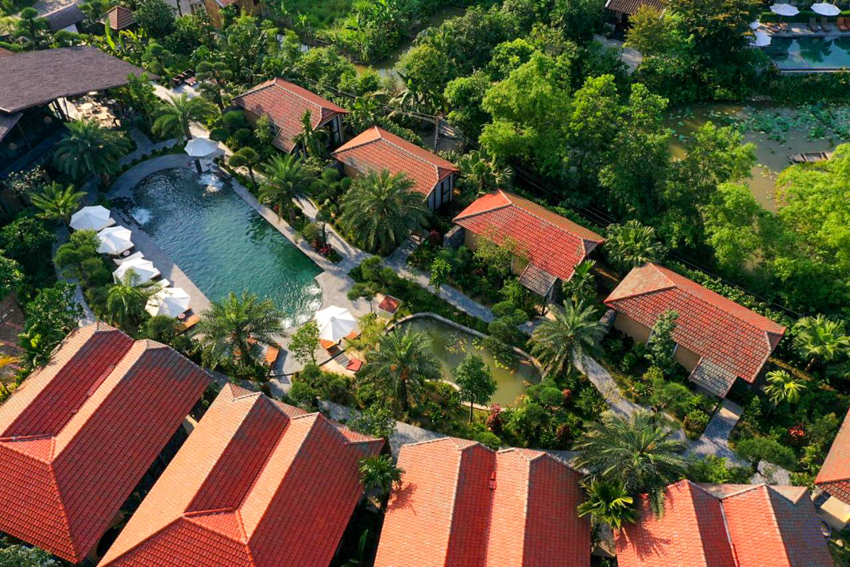 Aerial view of Tam Coc Retreat's red-roofed bungalows, lush gardens, and tranquil swimming pool.