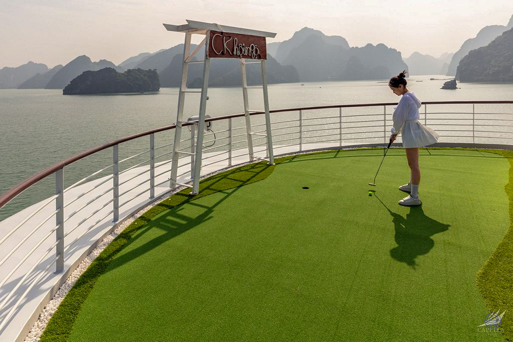 A woman enjoys a leisurely game of mini-golf on a cruise ship deck overlooking Halong Bay.