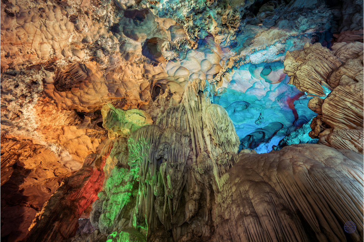 Colorful lights illuminate the stunning stalactites and cave formations inside a beautiful grotto in Ha Long Bay.