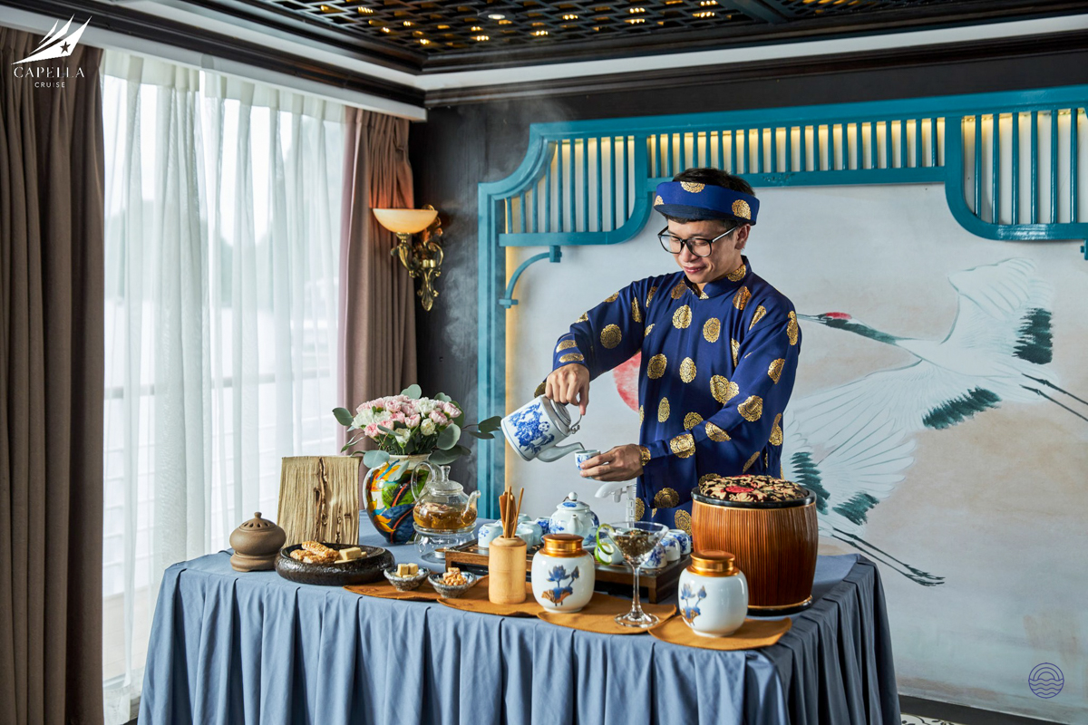 A man in traditional Vietnamese attire gracefully performs a tea ceremony on a cruise in Halong Bay.
