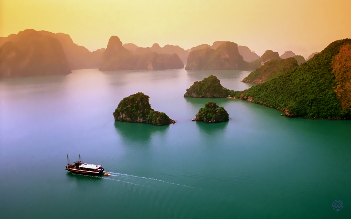 A traditional boat sails through the emerald waters of Ha Long Bay, surrounded by majestic limestone karsts.