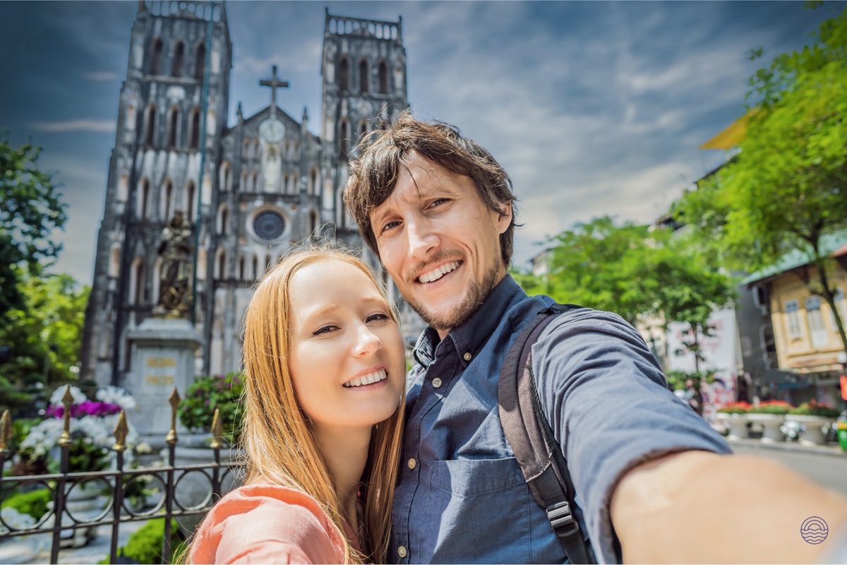 A joyful couple smiles for a selfie in front of Hanoi's historic St. Joseph Cathedral.