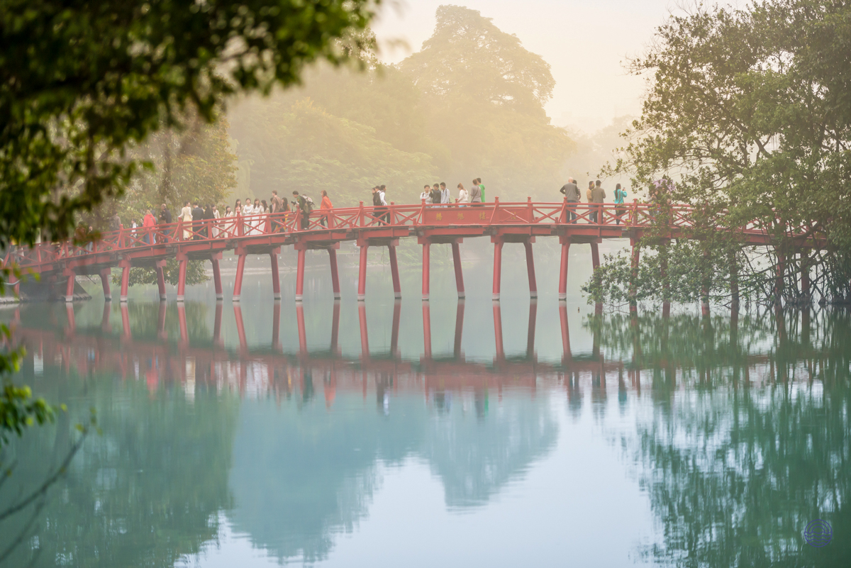People stroll across the iconic red Huc Bridge over Hoan Kiem Lake in misty Hanoi.