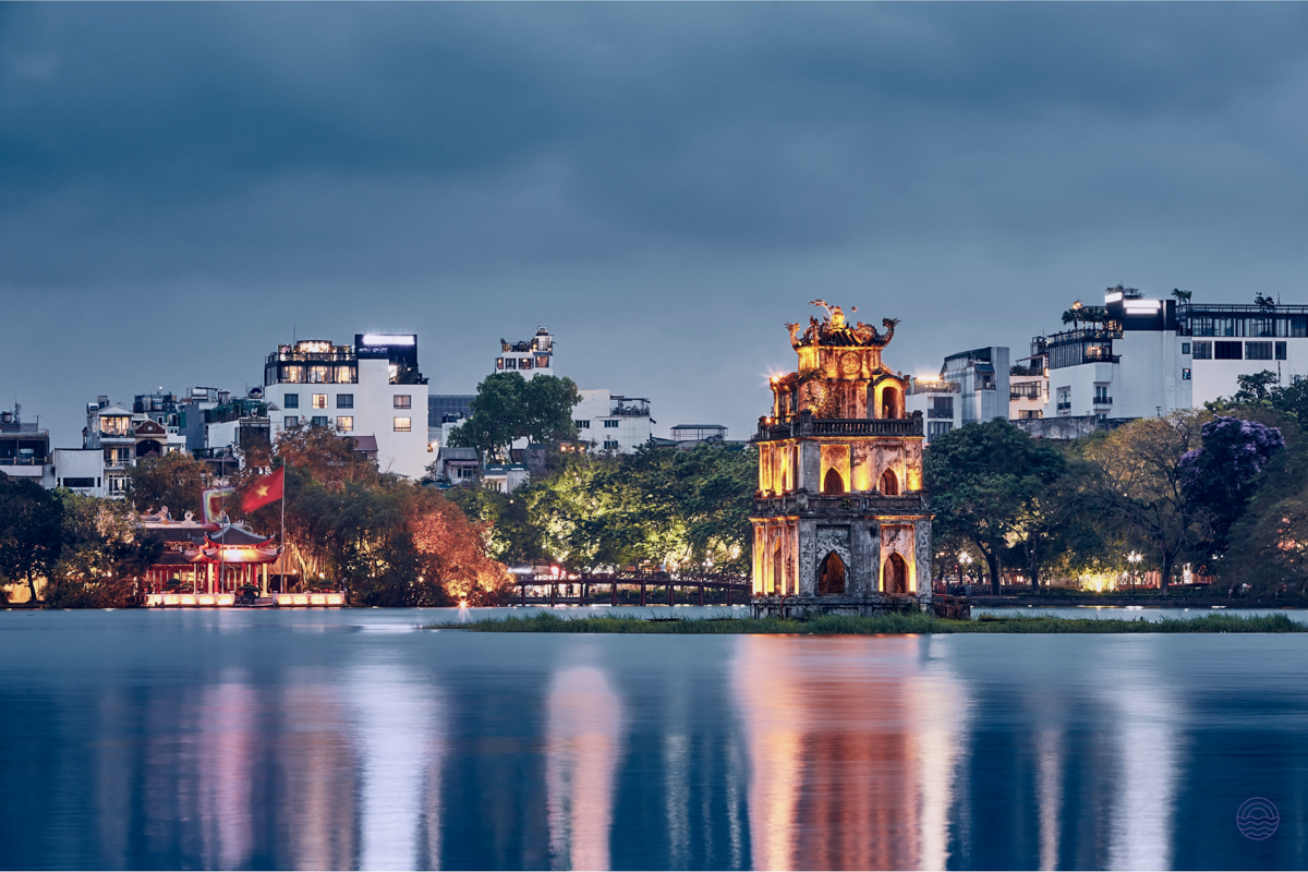 Historic Turtle Tower glowing with lights on Hoan Kiem Lake, reflecting beautifully in Hanoi at dusk.