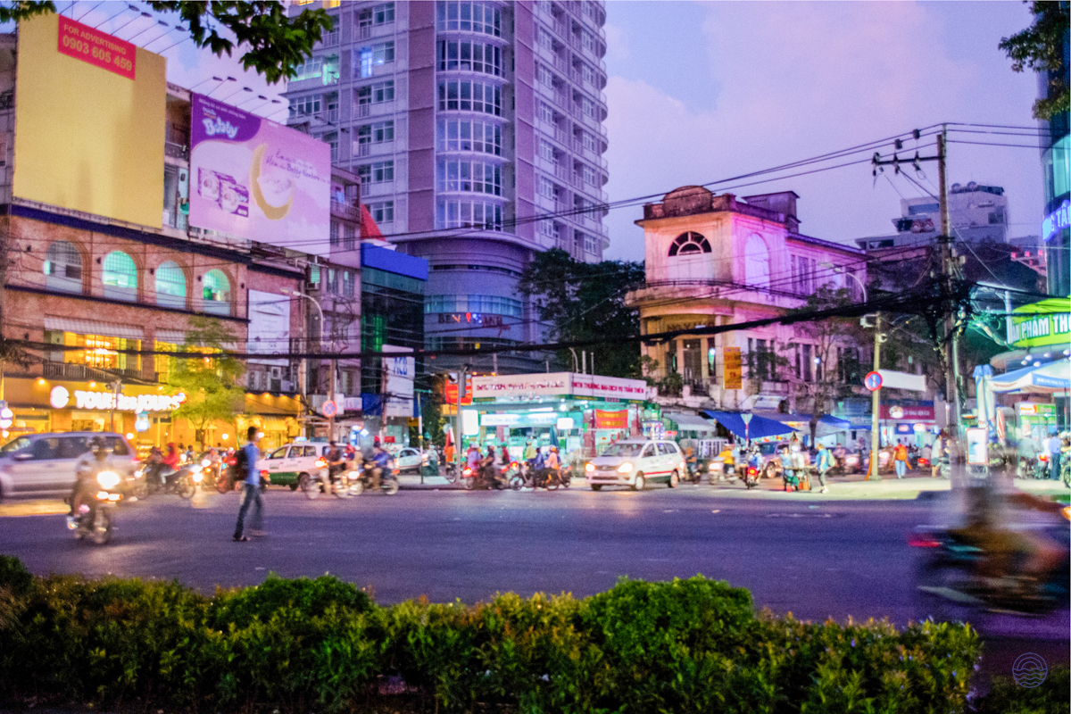A dynamic Ho Chi Minh City street scene at dusk, with busy traffic and colorful illuminated buildings.