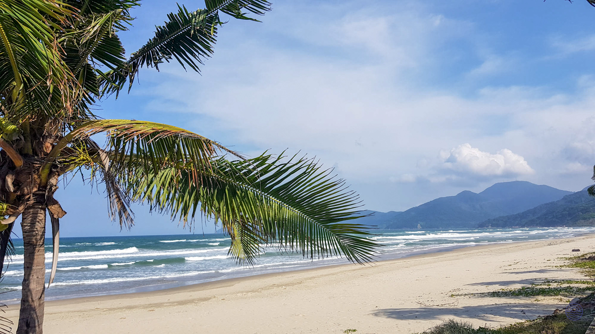 A tranquil view of An Bang Beach in Hoi An, with gentle waves, a sandy shore, and distant mountains.