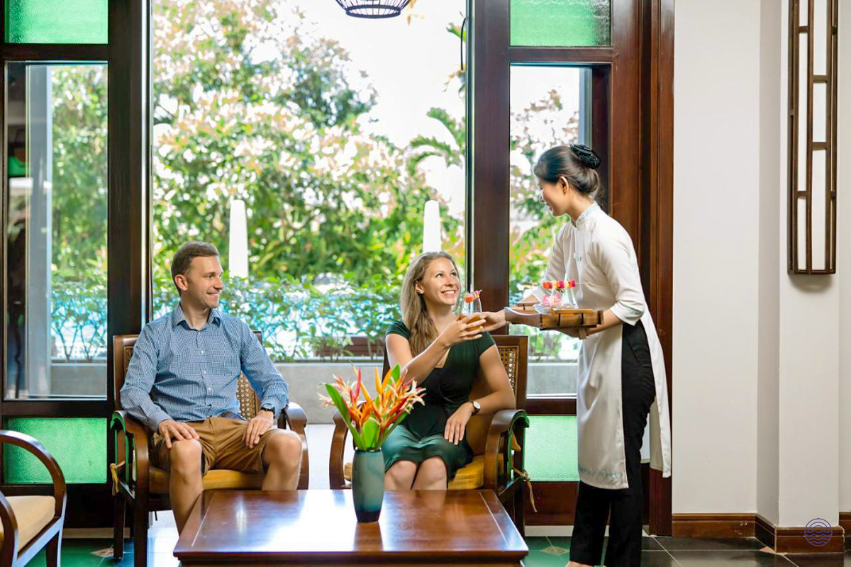A couple receives refreshing drinks from a hotel staff member in a welcoming lounge in Hoi An.