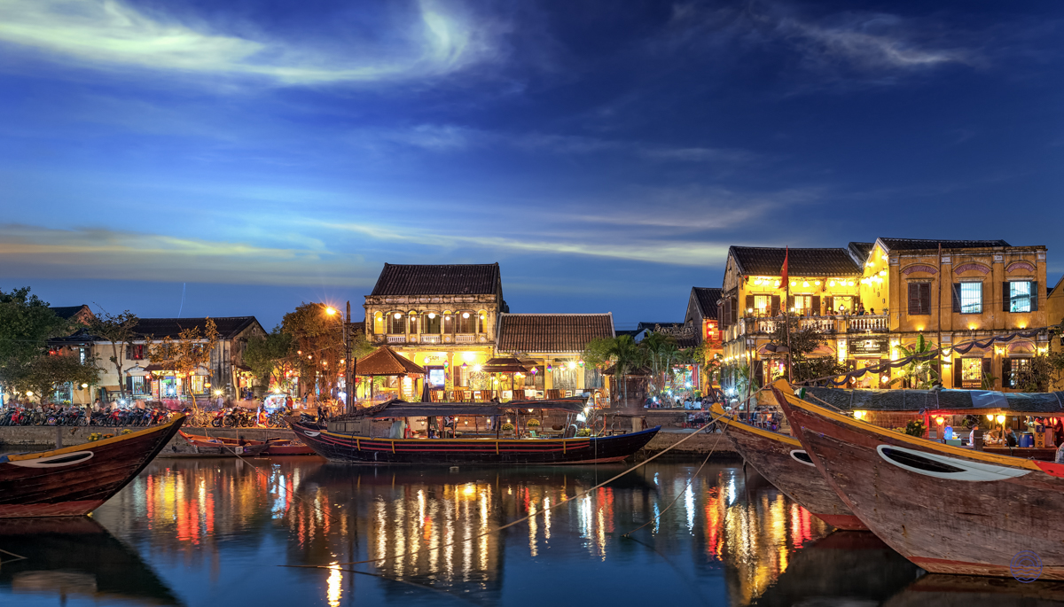 Hoi An's ancient town glows with warm lights at night, traditional boats reflecting in the tranquil river.