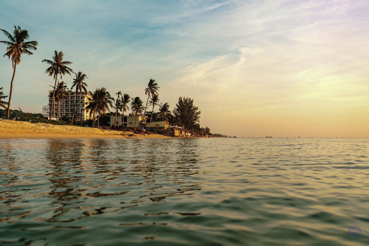 Sunset over a tropical beach in Phu Quoc, with calm waters, palm trees, and resort.