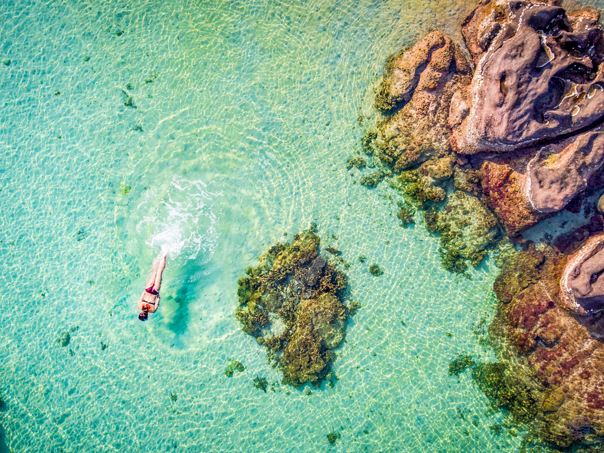 A person snorkeling in the vibrant, crystal-clear turquoise waters near rocky formations in Phu Quoc.