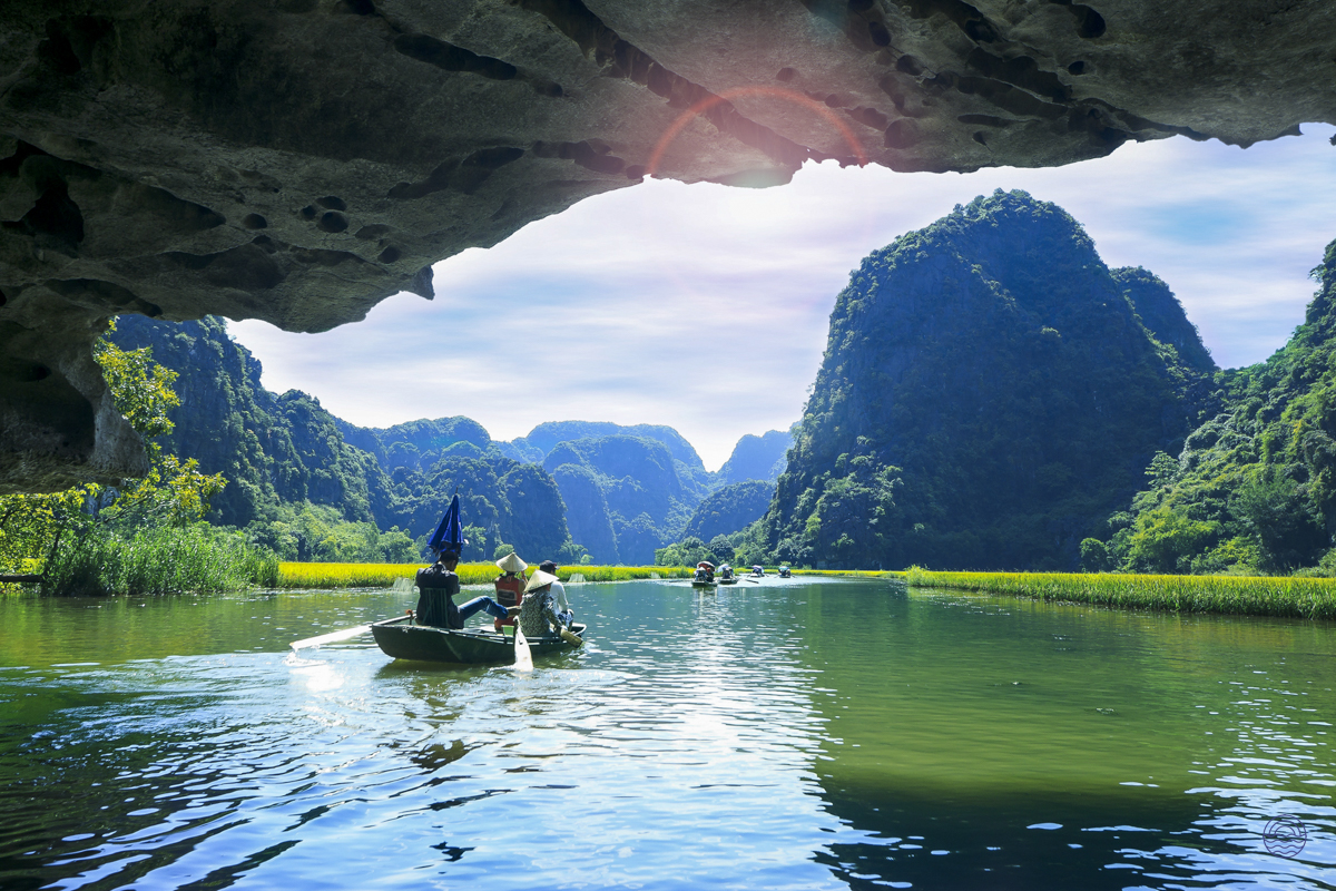 Boats navigate the serene river through Tam Coc's dramatic limestone karsts, seen from a cave.