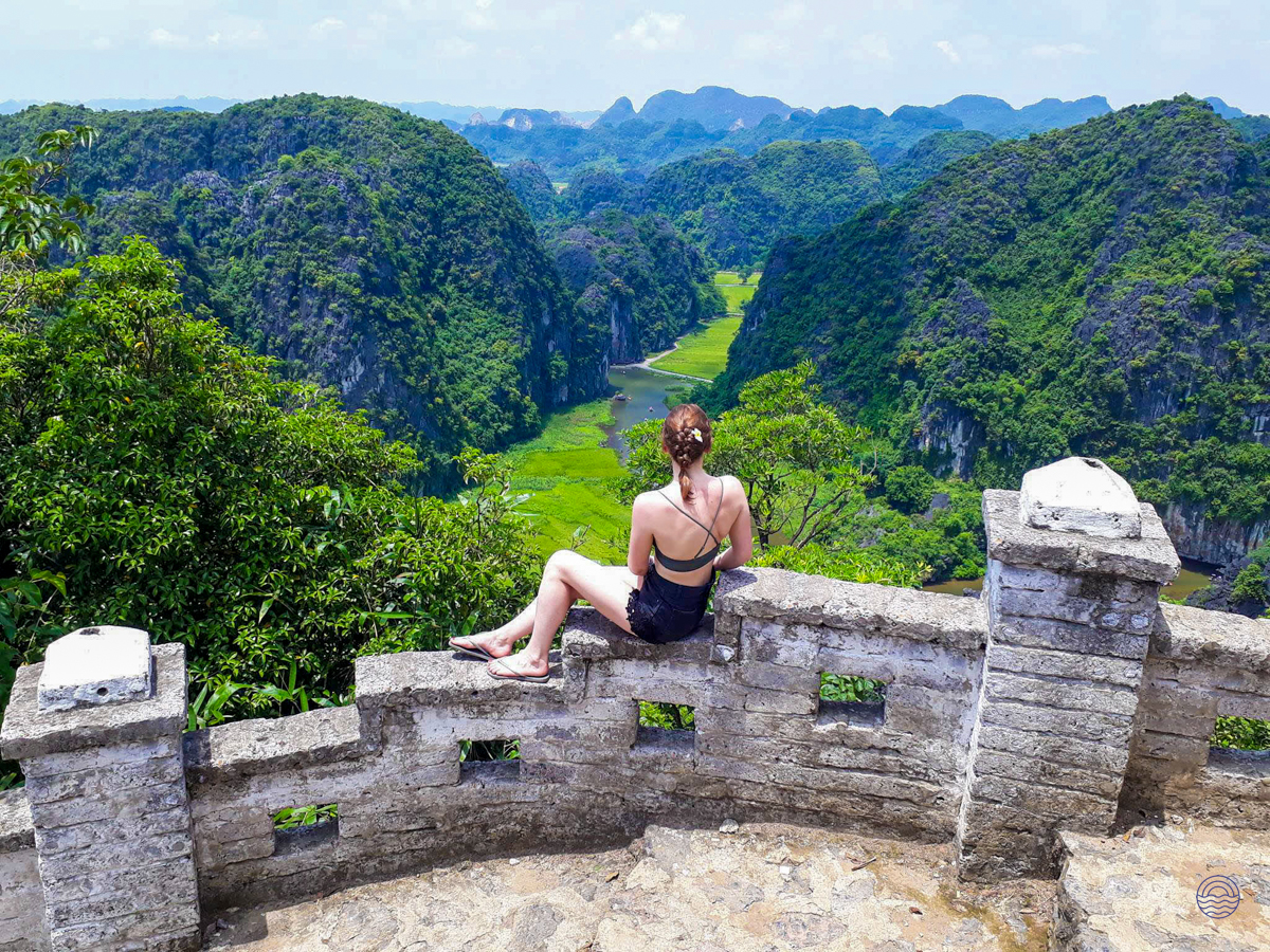 Woman gazing at the breathtaking panoramic view of Tam Coc's lush green mountains and winding river.