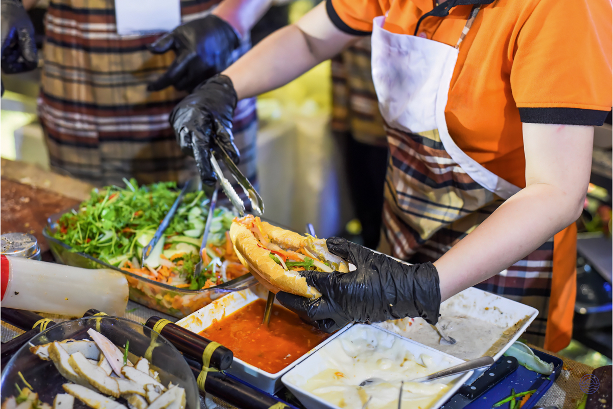 A vendor prepares a fresh banh mi sandwich with various ingredients in vibrant Ho Chi Minh City.