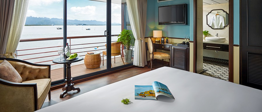 A luxurious cruise cabin featuring a comfortable bed and private balcony with serene Halong Bay views.