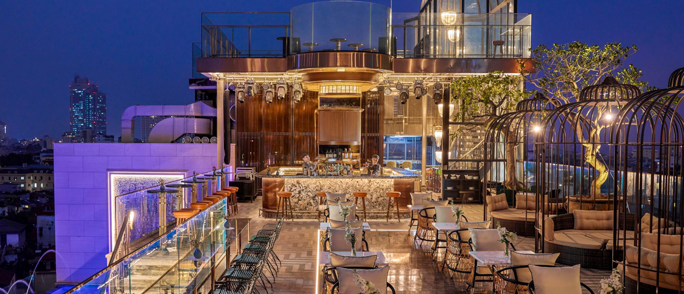 Luxurious rooftop bar in Hanoi with elegant seating, a vibrant bar, and unique birdcage lounges at dusk.