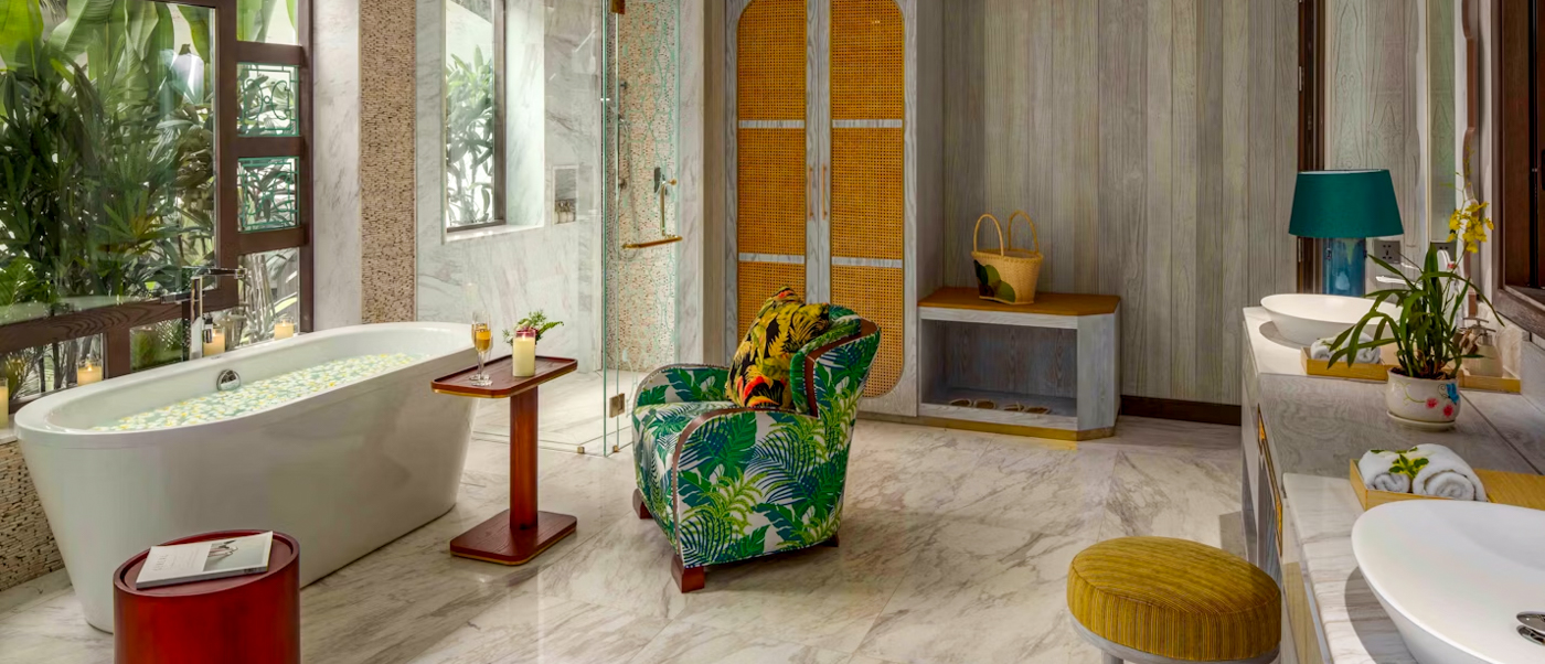 A luxurious bathroom in Ho Chi Minh City featuring a petal-filled bathtub and tropical-patterned armchair.