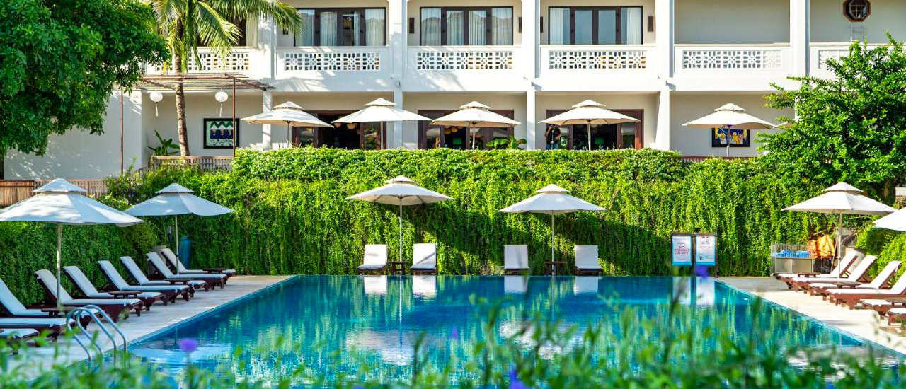 A tranquil resort swimming pool with lounge chairs and umbrellas, surrounded by lush greenery in Hoi An.
