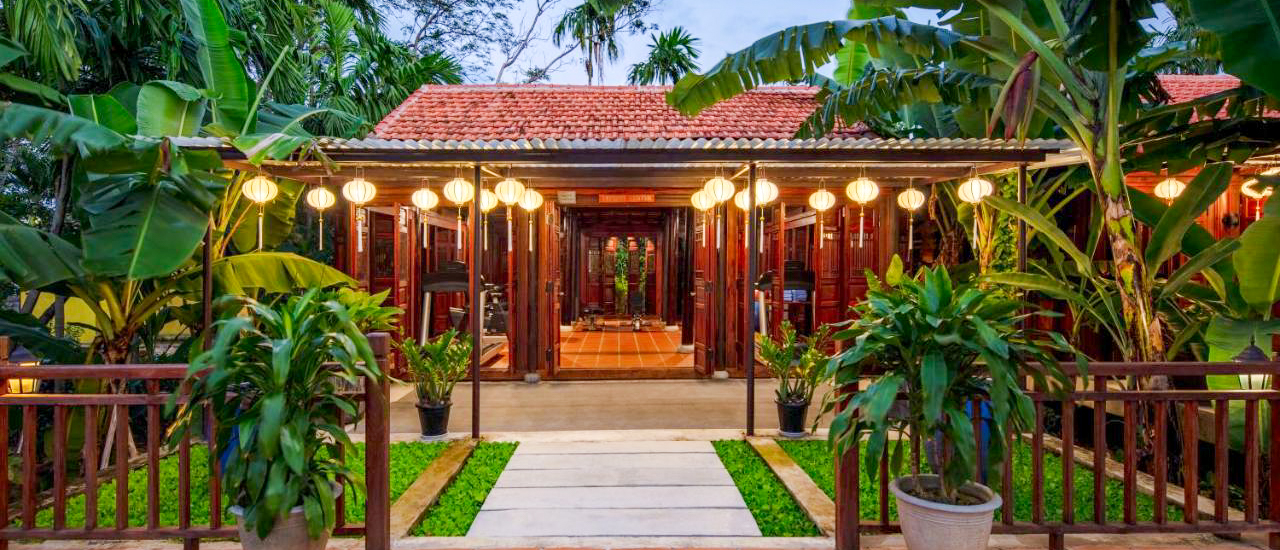 An inviting traditional Vietnamese building with a red tiled roof, lush plants, and glowing lanterns in Hoi An.