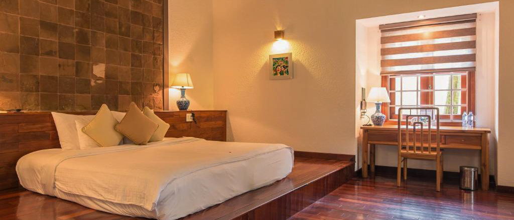 Serene resort room in Hue with a large bed, wooden floors, and a desk.