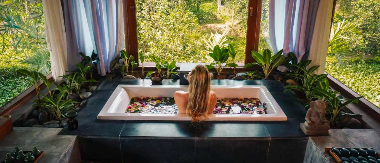 Woman relaxing in a luxurious flower-filled bathtub overlooking a lush tropical garden in Hue.