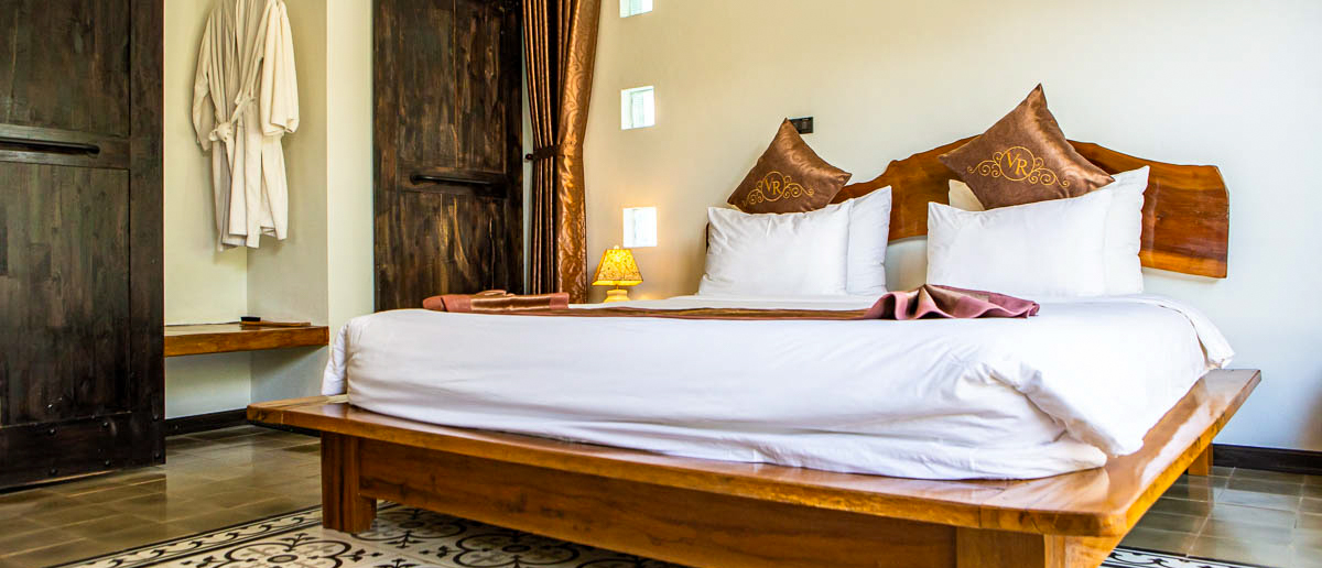 An inviting hotel bedroom featuring a large bed with white linens, wooden furniture, and a cozy lamp.