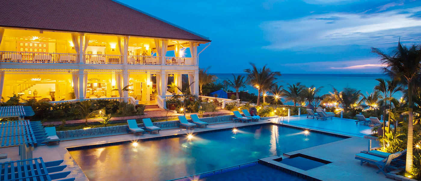 Luxurious resort building with a lit pool and palm trees overlooking the ocean at twilight in Phu Quoc.