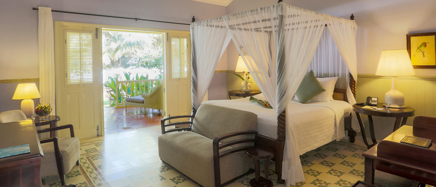 A luxurious hotel room in Phu Quoc with a four-poster bed and a balcony overlooking tropical greenery.