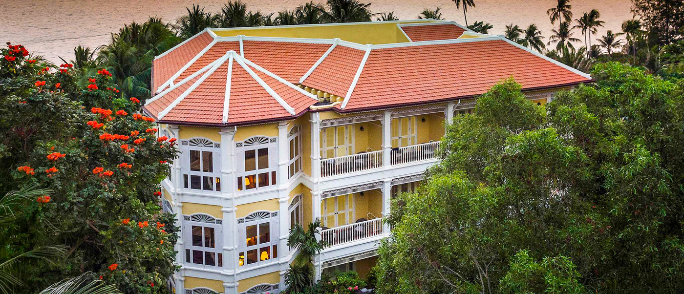 Elegant yellow hotel with red roof surrounded by lush tropical trees and flowering plants in Phu Quoc.