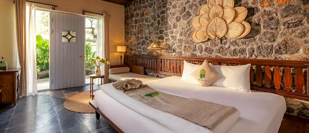 Inviting bedroom with a large bed, stone wall, and open door revealing lush greenery in Tam Coc.