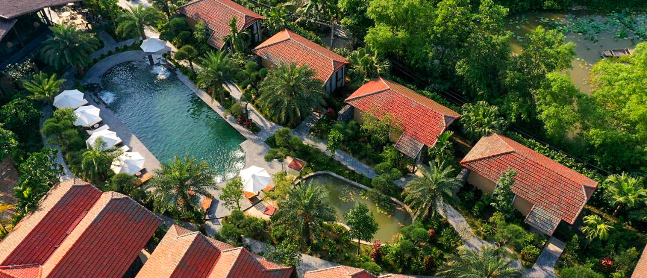 Luxurious Tam Coc retreat with a large swimming pool, red-tiled bungalows, and abundant tropical greenery.