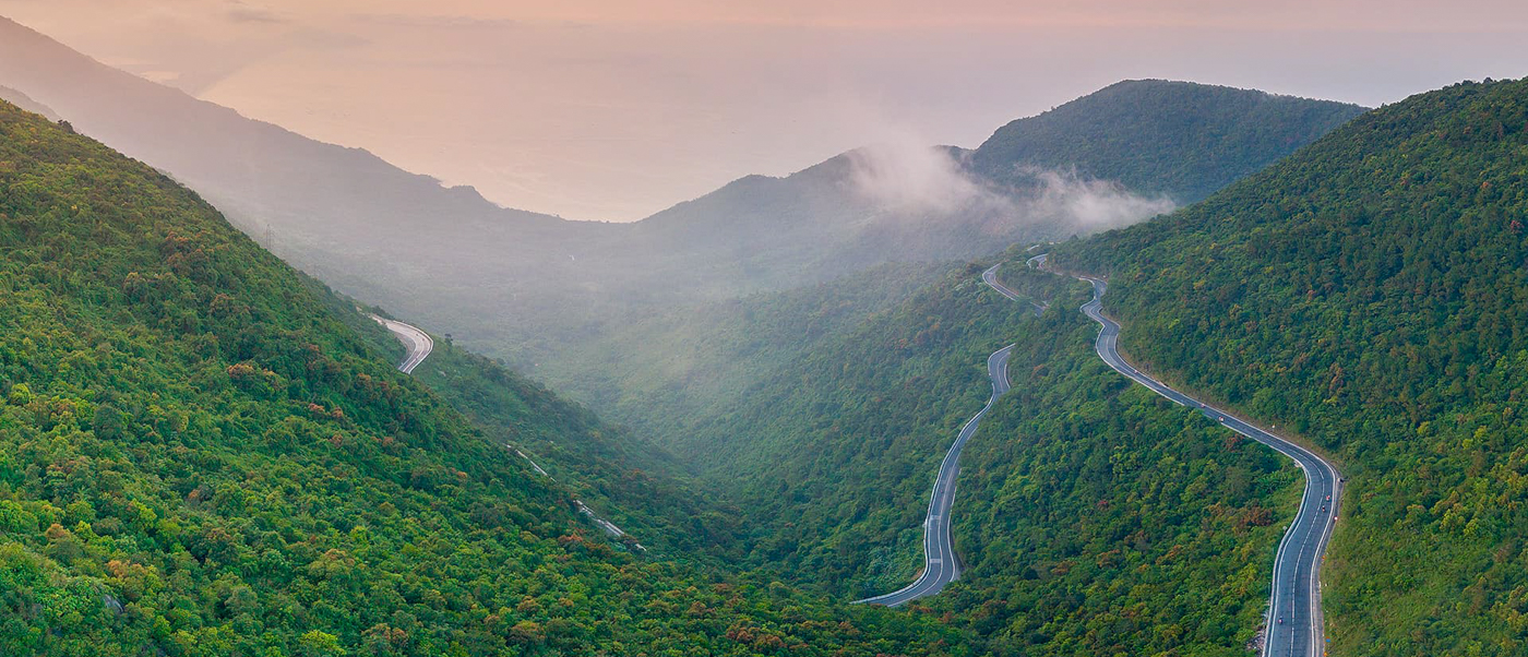 A dramatic winding road carves through verdant mountains and misty valleys on the Hai Van Pass.