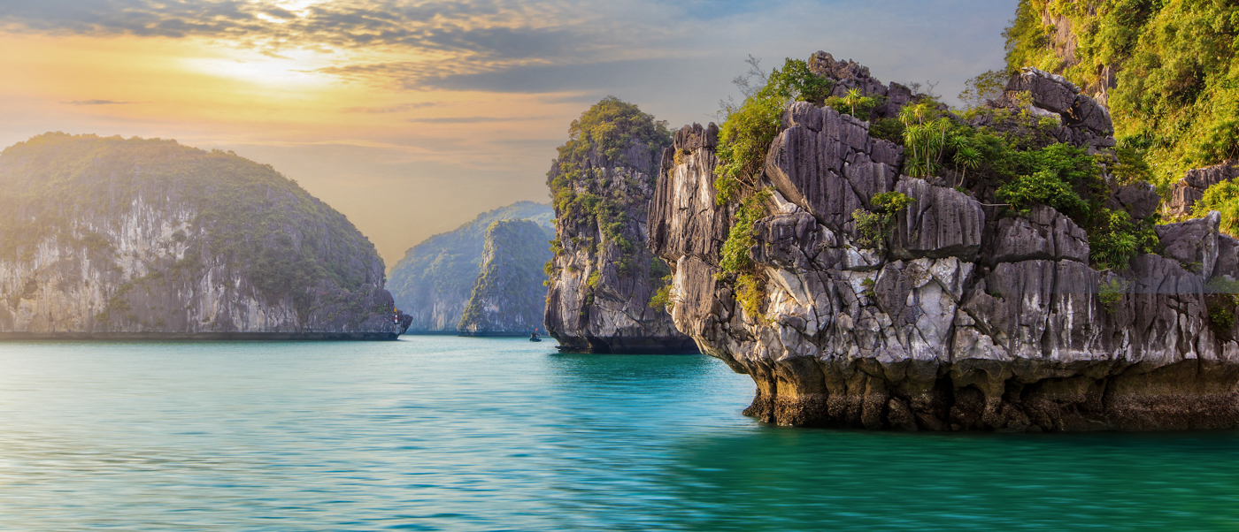 Majestic limestone karsts rise from emerald waters under a glowing sky in Ha Long Bay.