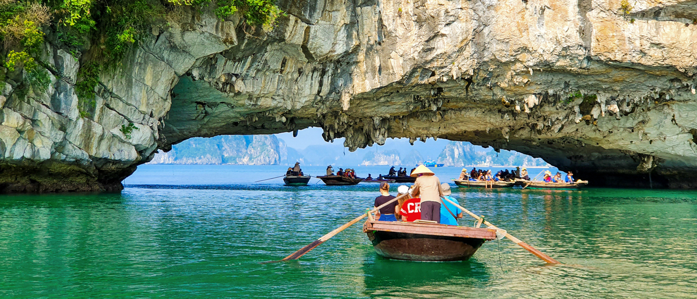 People in traditional boats explore the emerald waters and limestone archways of Halong Bay.
