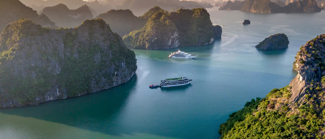 Two elegant cruise ships sail through the calm waters of Ha Long Bay, surrounded by majestic limestone islands.