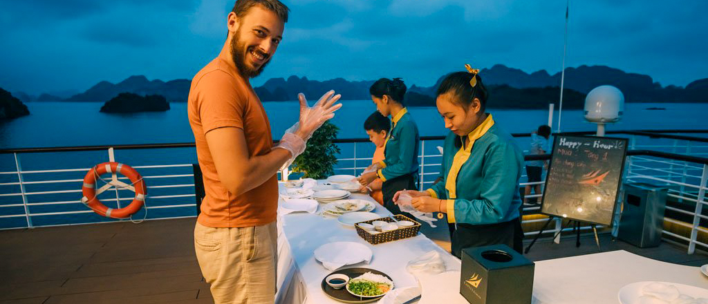 A smiling man and staff prepare food during a cooking class on a Halong Bay cruise.