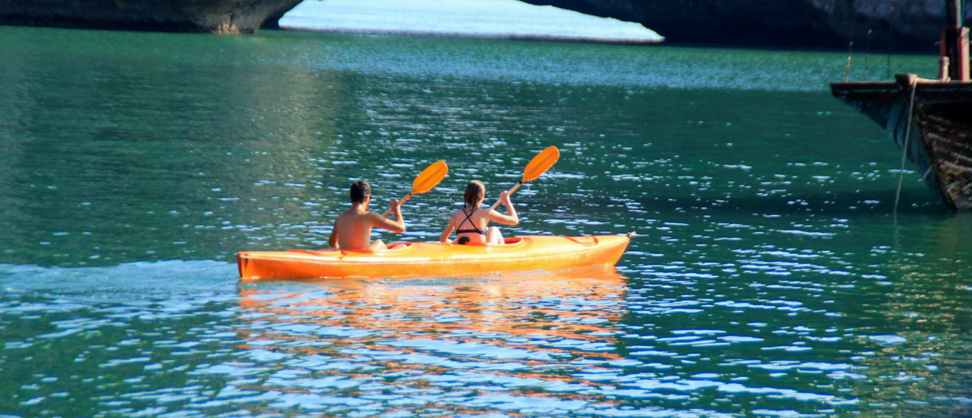 A couple paddles an orange kayak on the tranquil emerald waters of Halong Bay.