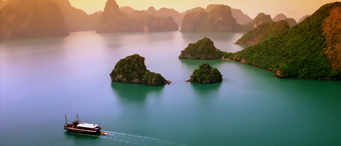 A traditional boat cruises through the emerald waters of Ha Long Bay, surrounded by majestic limestone karsts.