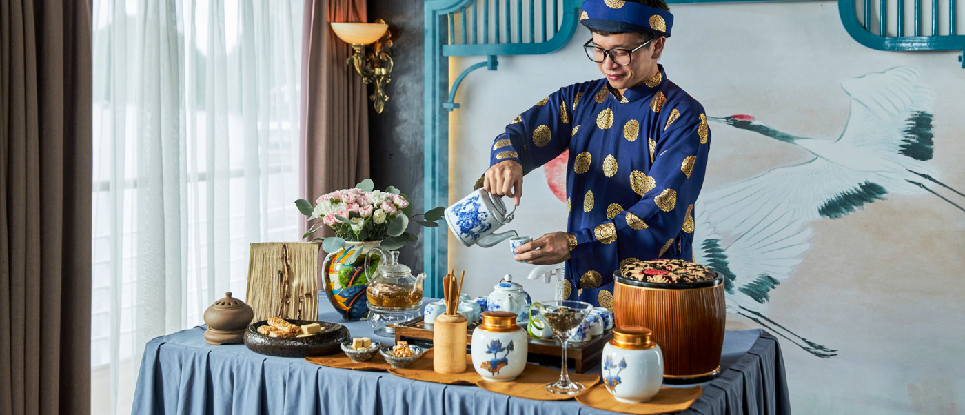 A person in traditional Vietnamese attire pours tea at an elegant ceremony in Halong Bay.