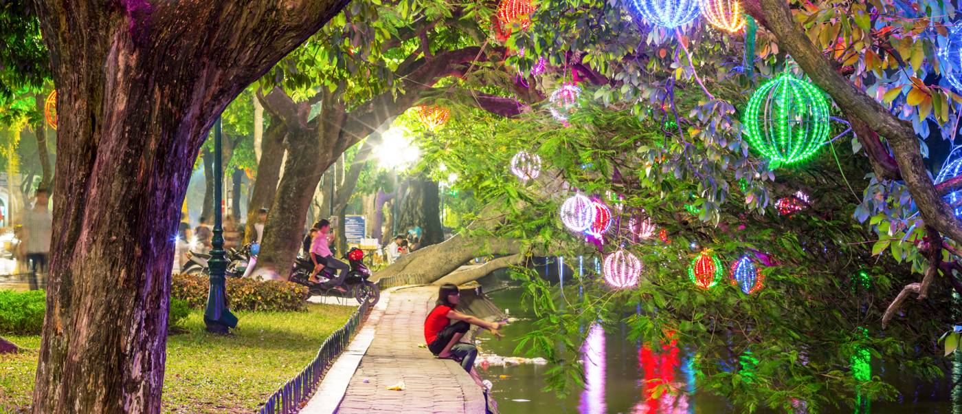 A lively evening in a Hanoi park, with trees illuminated by many colorful glowing lanterns.