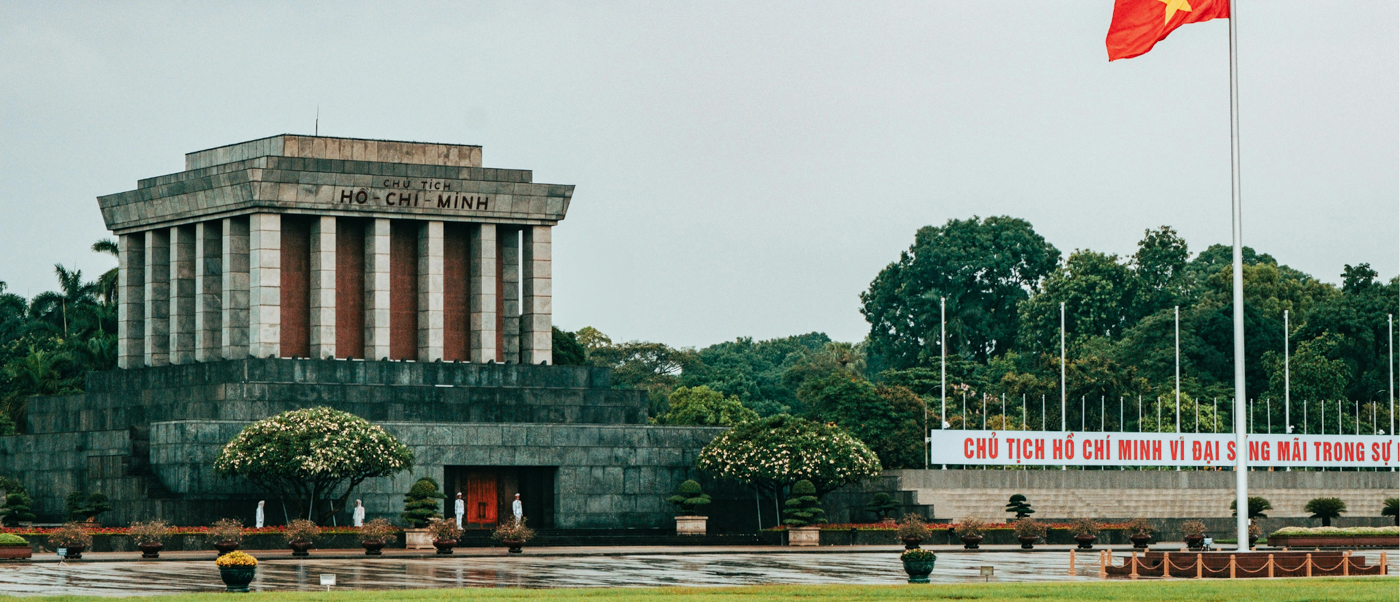 Ho Chi Minh Mausoleum in Hanoi with uniformed guards and a large Vietnamese flag flying.