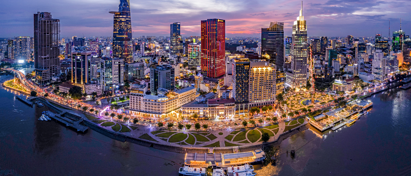 Ho Chi Minh City's bustling waterfront and illuminated skyline at twilight, reflecting in the river.