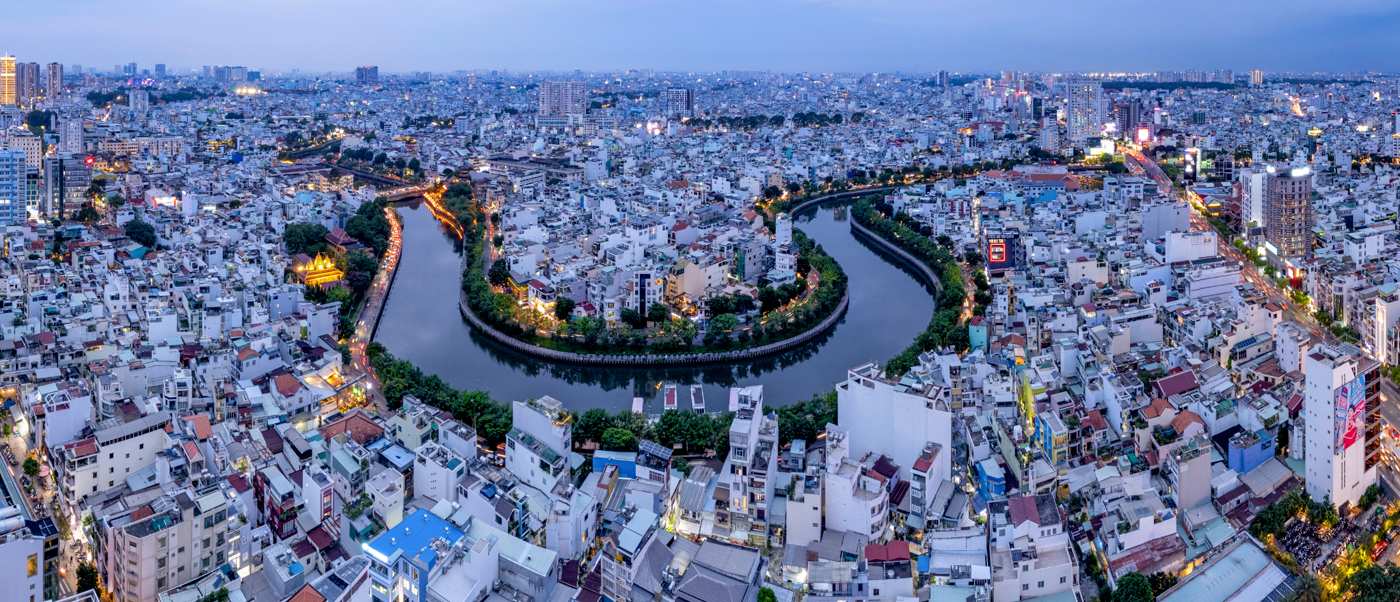 Aerial view of Ho Chi Minh City at dusk, a winding river flowing through countless illuminated buildings.