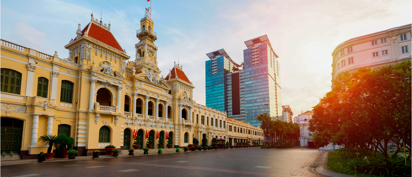 Historic Ho Chi Minh City Hall, a grand yellow building, stands proudly beside modern glass skyscrapers.