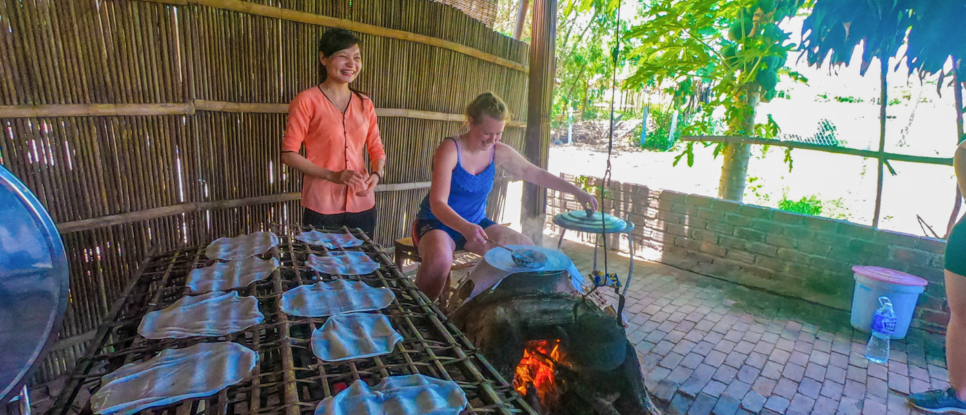 A tourist and a local woman happily prepare traditional food during a cooking lesson in Hoi An.