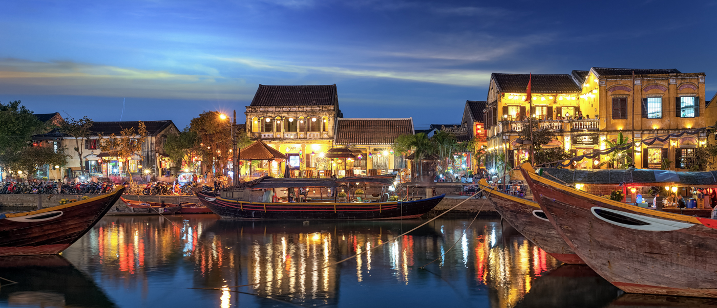 Lively night scene along Hoi An's river, with illuminated buildings, traditional boats, and vibrant reflections.
