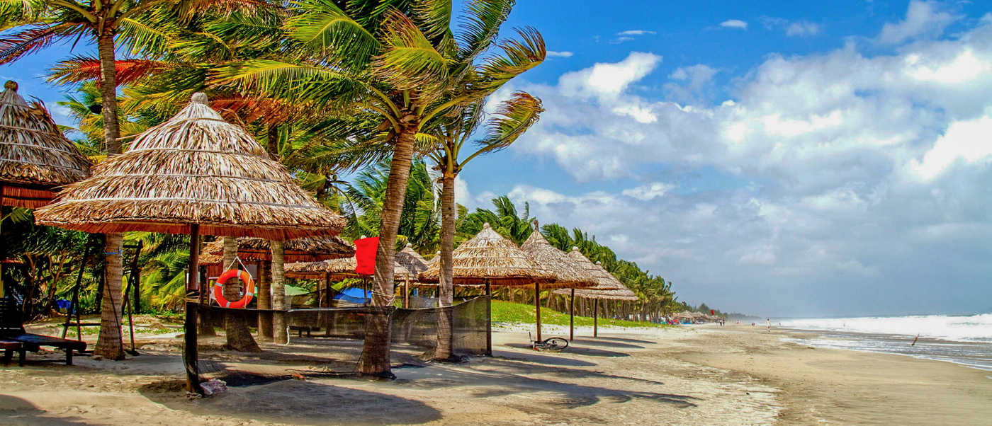 Tropical beach with palm trees, thatched umbrellas, and gentle waves on the sandy shore of Thuan An Beach.