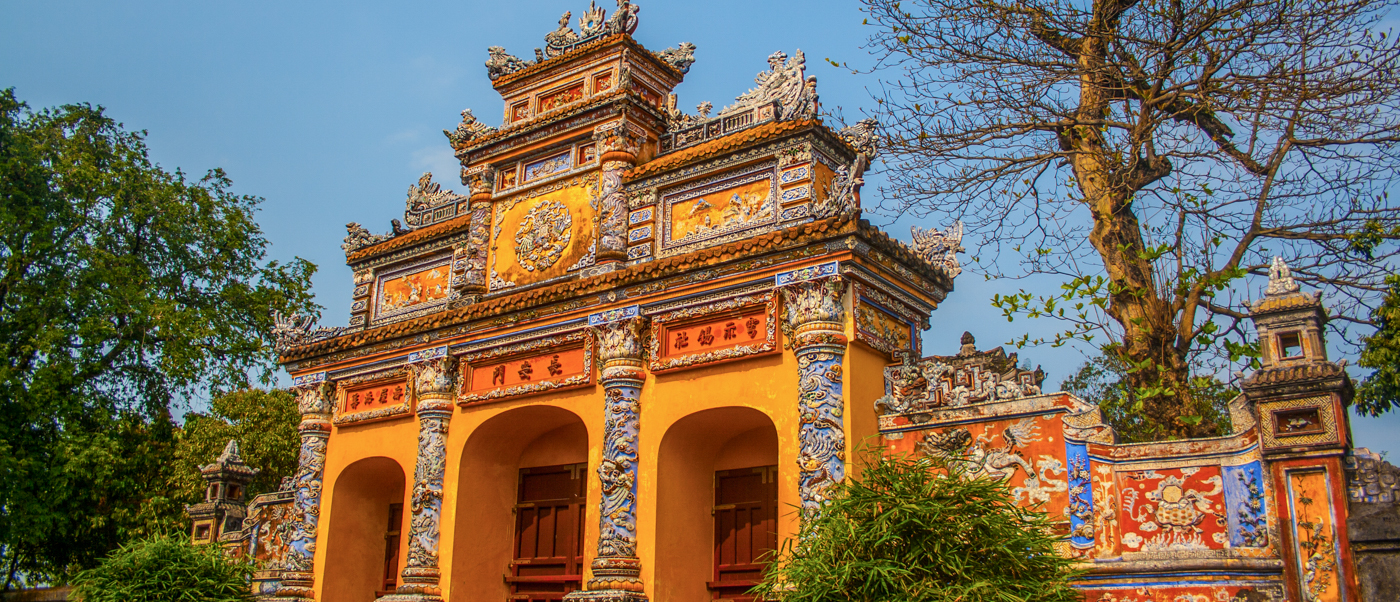 Ornate yellow and orange gate of Hue's Imperial Citadel with intricate details under a clear blue sky.